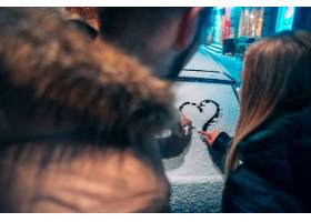 年轻的成年夫妇在积雪覆盖的汽车上画下了一_613605201