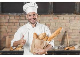 面带微笑的年轻男面包师拿着纸袋里的面包_2966199