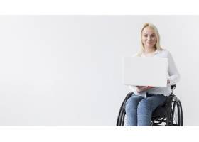 坐在轮椅上的微笑女子在笔记本电脑上工作的_7772362