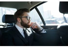 一名戴眼镜的男子坐在汽车后座上_7858077
