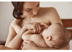 早晨年轻的裸体母亲抱着坐在床上的新生儿_9321526