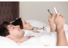 幸福的年轻夫妇在床上使用智能手机的侧观_3955557