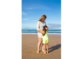 快乐的妈妈和可爱的小女儿穿着夏装站在海边_10608461