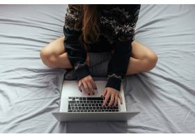 女性盘腿坐在床上用笔记本电脑打字_13006861