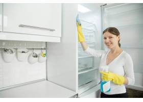 戴着橡胶手套的年轻微笑着的女人在打扫冰箱_1281452