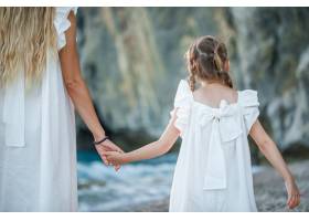 幸福的母女俩身着白裙在日落时分站在海边_9178892