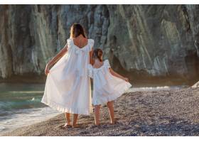 幸福的母女俩身着白裙在日落时分站在海边_9178909
