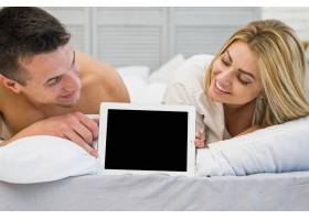 快乐的女人和年轻的微笑男人在床上带着相框_3553516