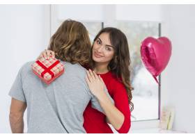 一位微笑的年轻女子拿着红色礼盒拥抱她的男_3836217
