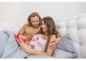 一名男子看着他的女朋友拿着躺在床上的红色_3836207