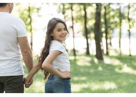微笑的女孩和她的父亲在公园散步时看着相机_4958751