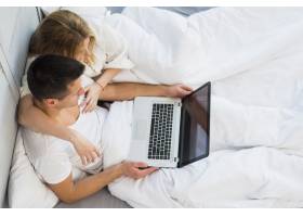 年轻夫妇在床上用毯子盖着笔记本电脑_3524214