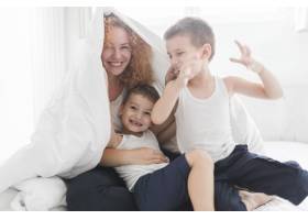快乐的女人裹着毯子和她的儿子们玩耍_3143533