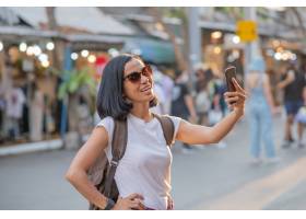 使用手机的愉快的年轻旅行亚裔妇女和在街道_13807789