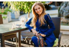 微笑的美丽的妇女在坐在咖啡馆的典雅的蓝色_13868813