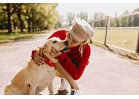 亲吻她的狗的可爱的白肤金发的狗在秋天公园_12018417