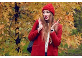 摆在秋天公园的红色帽子和夹克的愉快的白肤_9419160