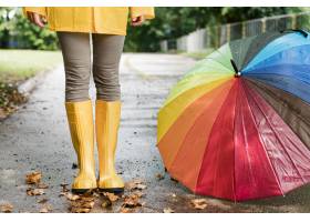 站立在五颜六色的伞旁边的雨靴的妇女