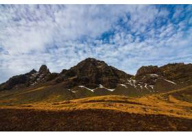 在绿叶和雪盖的岩石风景在多云天空下在冰岛