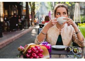 坐在咖啡馆的年轻时髦的妇女拿着杯热奶咖_9644110