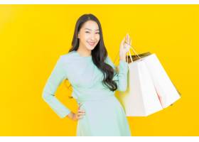 画象美丽的年轻亚裔妇女微笑与在黄色的购物_15401830