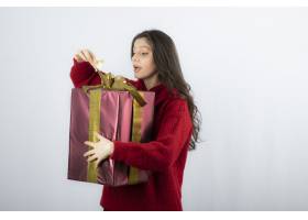 穿着红色毛衣的惊讶女人打开了一盒圣诞礼物