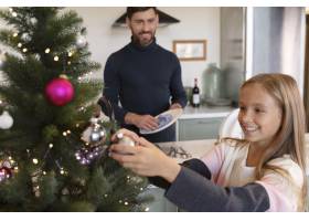 女孩在装饰圣诞树而她的父亲正在洗碗