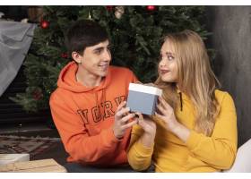 快乐的男人在圣诞树旁给他的女朋友圣诞礼物