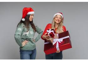 两位女朋友在灰色背景上拿着圣诞礼物并留