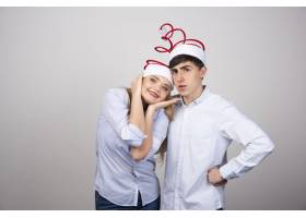 这对可爱的年轻夫妇戴着圣诞老人帽站在灰色