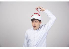 年轻人触摸灰色墙上的红色圣诞老人帽子