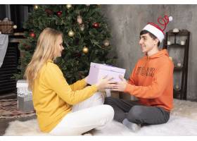 年轻可爱的女朋友在圣诞树旁向男朋友赠送礼