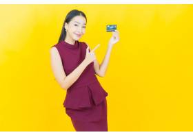 黄墙上一位年轻美丽的亚洲女子用信用卡微